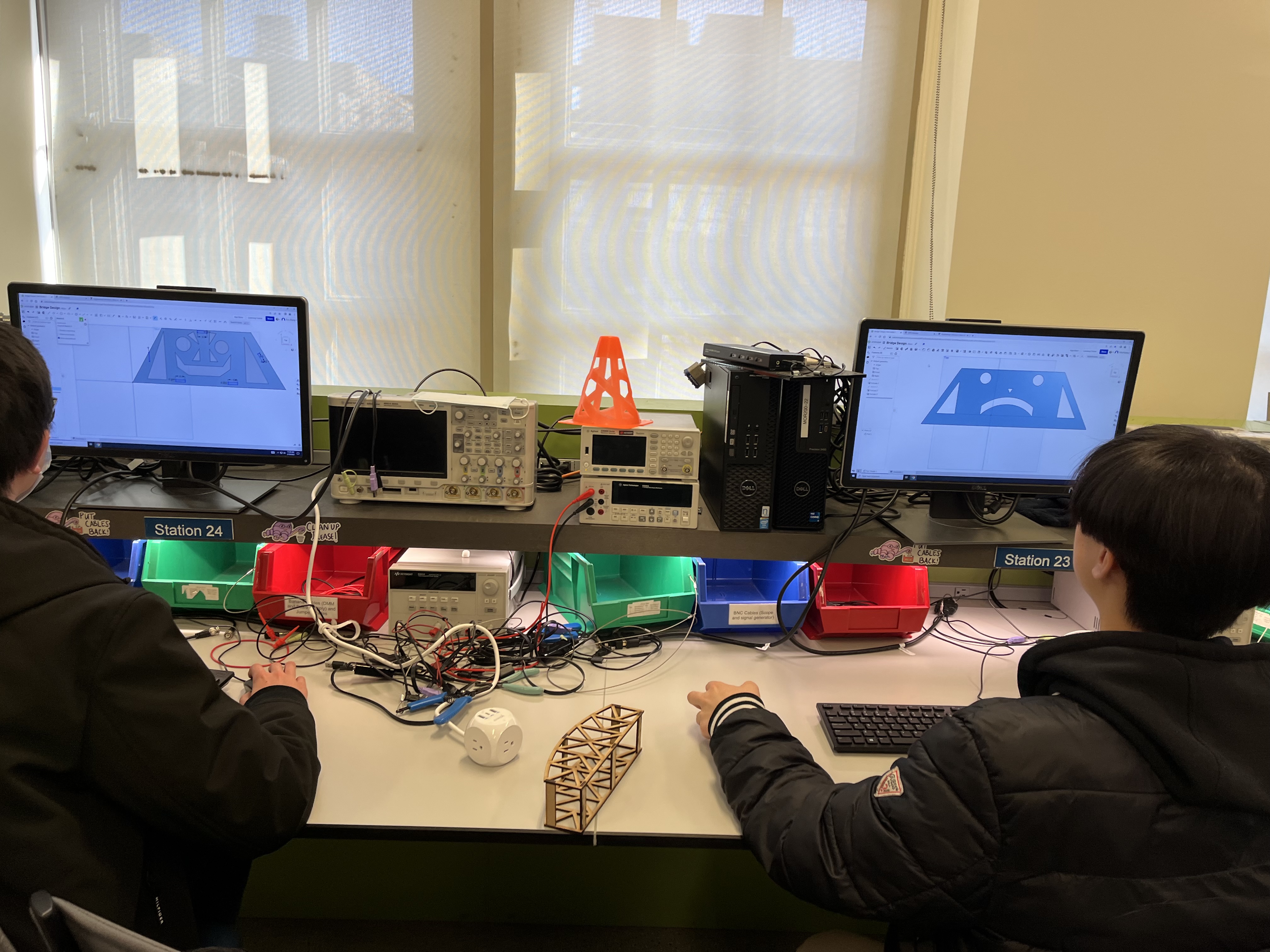 Two students at computers with a laser-cut model bridge on the desk